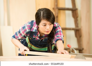 Skilled Carpenter Cutting A Piece Of Wood In Her Woodwork Workshop, Using A Circular Saw. Mixed Race Asian Chinese Model.