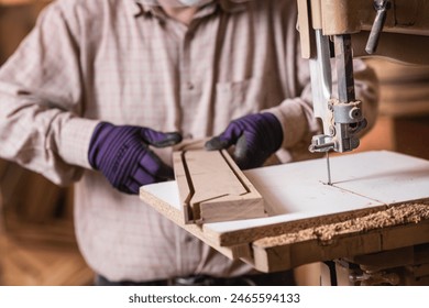 Skilled carpenter using band saw machine, wearing safety gloves in carpentry workshop - Powered by Shutterstock