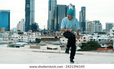Skilled caucasian B-boy dancer practicing street dancing at rooftop with city sites or urban. Motion shot of young man performing street dance by doing freeze pose. Outdoor sport 2024. Endeavor.