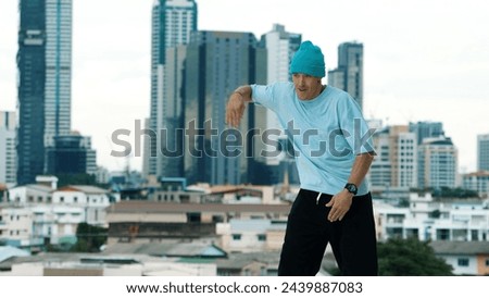 Skilled caucasian B-boy dancer practicing street dancing at rooftop with city sites or urban. Motion shot of young man performing street dance by doing freeze pose. Outdoor sport 2024. Endeavor.