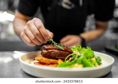 A skilled chef artfully garnishes a perfectly grilled steak with fresh herbs, elegantly plated on white porcelain - Powered by Shutterstock