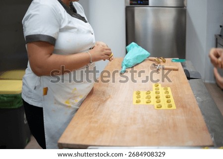 Skilled chef meticulously preparing fresh pasta dough in a clean commercial kitchen environment using a pastry bag and specialized tools to create delicate ravioli shapes on a wooden surface