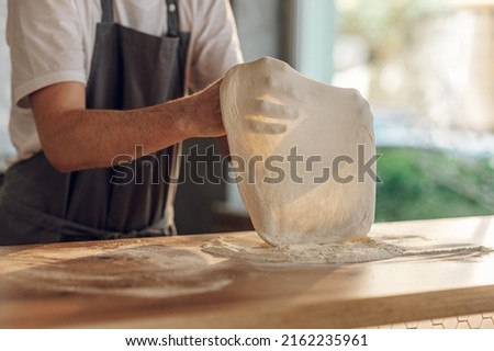 Skilled chef preparing dough for pizza rolling with hands while working in a pizza place. The process of making pizza.Focus on a man hands.