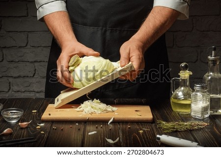 A skilled chef slices a head of cabbage with a handheld slicer on a wooden cutting board. The rustic kitchen includes various herbs and ingredients around, creating a vibrant cooking atmosphere.