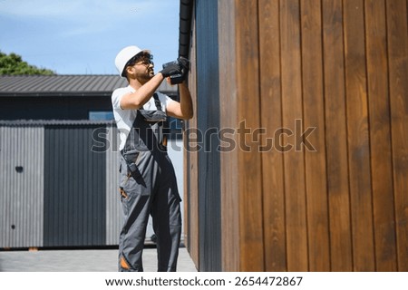 Skilled construction worker using power tool to install wooden panels on prefabricated building, ensuring precise and secure attachment