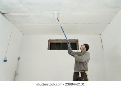 A skilled craftsman meticulously paints a pristine white ceiling using a telescopic roller for precise home improvement.