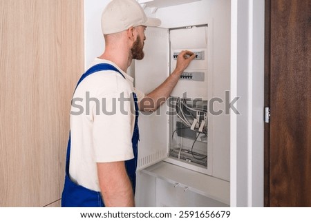 A skilled electrician is checking the electrical panel in a residential apartment, ensuring the connections are secure and functional for optimal energy efficiency.