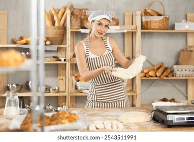 Skilled female baker in striped apron kneading dough on flour-dusted wooden table in cozy inviting setting of small artisan bakery, highlighting craftsmanship of traditional breadmaking - Powered by Shutterstock