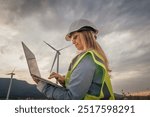 A skilled female engineer is conducting vital research at a modern wind farm, using advanced technology on her laptop to improve sustainability and drive innovation in engineering