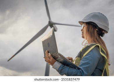 A skilled female engineer monitors wind turbines on her laptop, crucial in developing sustainable energy solutions and advancing technology and infrastructure for a cleaner future - Powered by Shutterstock