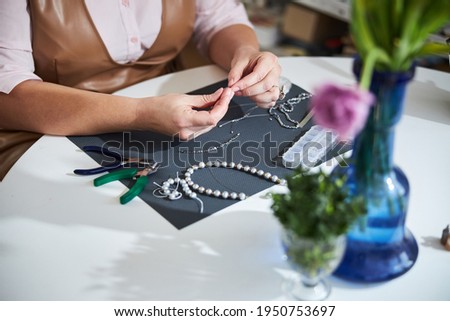 Skilled female jeweler stringing beads at the table