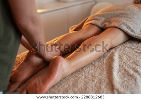 Skilled female masseur giving leg massage to young female.