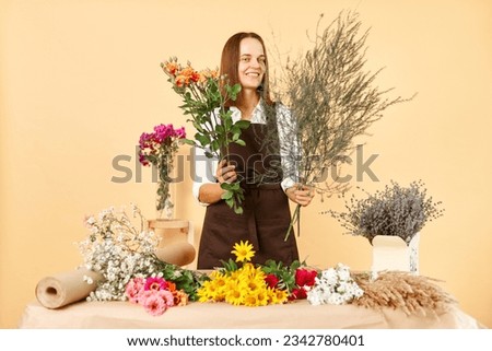 Skilled floral designers at work. Assorted bouquets for every occasion. Delicate flower decoration service. Woman florist in brown apron making bouquet of fresh flowers isolated over beige background