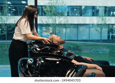 Skilled hairstylist tenderly rinses a clients hair from shampoo with warm water at modern barbershop. - Powered by Shutterstock