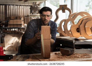 Skilled male carpenter focused on woodworking in workshop, shaping wood by hand for custom guitar crafting. Traditional craftsmanship with tools, dust, and dedication in creative workspace - Powered by Shutterstock - Get 15% off with code: PIKWIZARD15