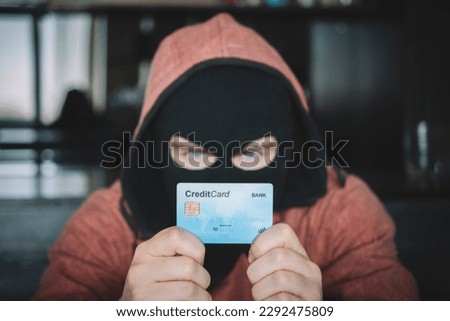 Skilled masked criminal using a stolen credit card to buy things online. A thief in a black mask holds a stolen bank card in his hands. Foto stock © 
