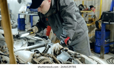 Skilled mechanic checking car engine with flashlight, wearing protective gloves during diagnostic evaluation in professional automotive workshop