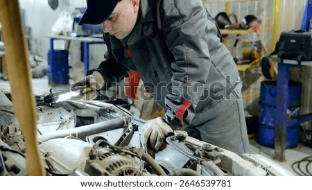 Skilled mechanic checking car engine with flashlight, wearing protective gloves during diagnostic evaluation in professional automotive workshop