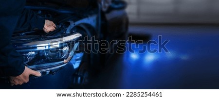 Skilled mechanic workInstalling new front headlight on a car with precision and expertise. Working in garage or auto service center. Detail shot of process with focus on a mechanic hands and tools.