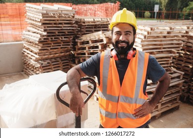 Skilled People Working In Construction Site. Hispanic Man At Work In New House. Portrait Of Happy Latino Worker Using Manual Forklift To Move Hardware And Smiling At Camera