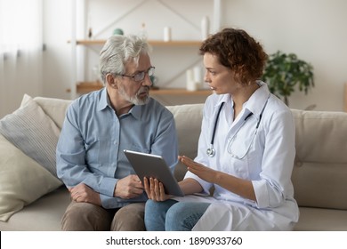 Skilled professional physician doctor prescribing illness treatment, showing health test results on digital computer tablet to concentrated older retired patient at home, sitting together on sofa.