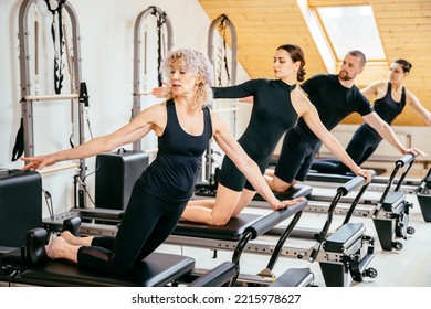 Skilled senior female trainer woman in front split on pilates reformer during class while adjusts form trains young instructors in studio. Rehabilitation, healthy lifestyle, small business concept. - Powered by Shutterstock