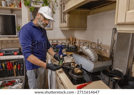 Skilled technician inspecting a kitchen extractor hood circuit board during home appliance maintenance, using professional tools and protective gloves for precise repair work.