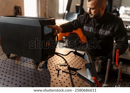 Skilled technician operating a high tech laser welding machine, adjusting settings on the control panel while working on a metal project in a modern industrial workshop
