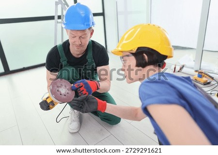 A skilled tradesman and eager learner engage in hands-on education, examining tools in a bright, contemporary workshop filled with equipment, showcasing teamwork and growth.