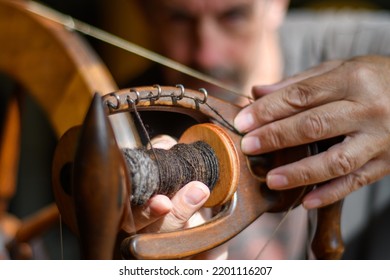 Skilled tradesman works to repair and to intricately fettle the mechanism of an old wooden spinning wheel. Selective focus to accentuate the task of repair and service. Contrasting lighting - Shutterstock ID 2201116207