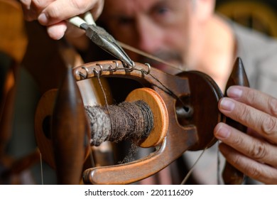 Skilled tradesman works to repair and to intricately fettle the mechanism of an old wooden spinning wheel. Selective focus to accentuate the task of repair and service. Contrasting lighting - Shutterstock ID 2201116209
