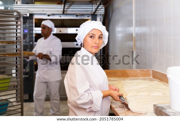 Skilled woman\
baker dividing raw dough into equal portions and weights them.\
Process of making bread in\
bakery