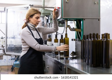 Skilled woman engaged in olive oil production, controlling process of bottling of finished product in glass bottles - Powered by Shutterstock