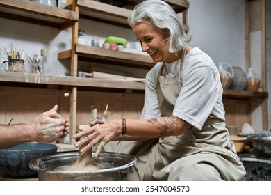 A skilled woman with silver hair expertly molds clay while smiling in her creative workspace. - Powered by Shutterstock