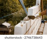 A skilled worker builds a solid wall using concrete bricks at a construction site for a new home. Focused on precision, the process shows careful craftsmanship.