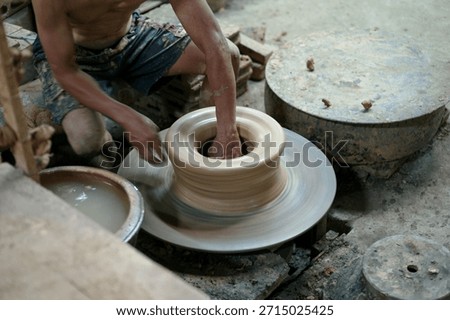 The skilled worker doing the clay work on the spinning wheel for modeling the shape of jar.