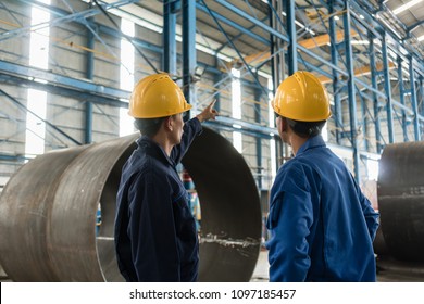 Skilled Worker Pointing Up While Giving Instructions To An Apprentice In A Factory Manufacturing Boilers