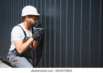 Skilled worker using cordless drill to install metal siding, focusing on precision and safety in building construction