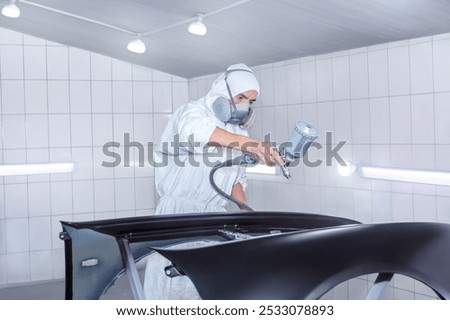 Skilled worker using spray gun to paint car body in workshop. for automotive repair, vehicle customization, or industrial craftsmanship concepts.