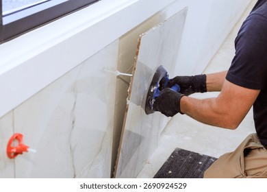 Skilled worker using vacuum suction cup tool tile piece to fit into wall in contemporary indoor space.