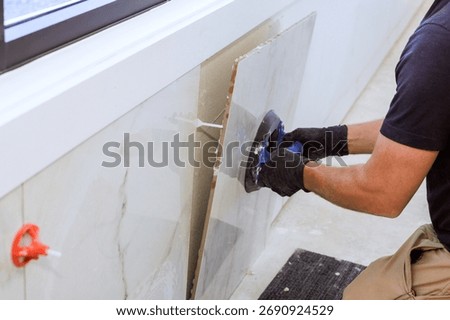 Skilled worker using vacuum suction cup tool tile piece to fit into wall in contemporary indoor space.