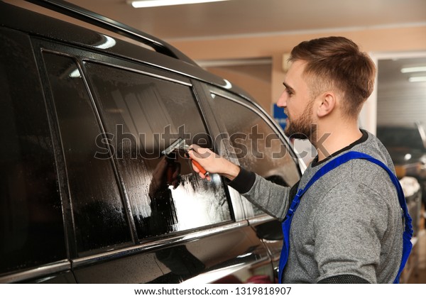 Skilled worker\
washing tinted car window in\
shop