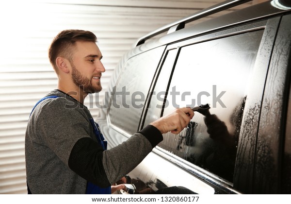 Skilled worker\
washing tinted car window in\
shop