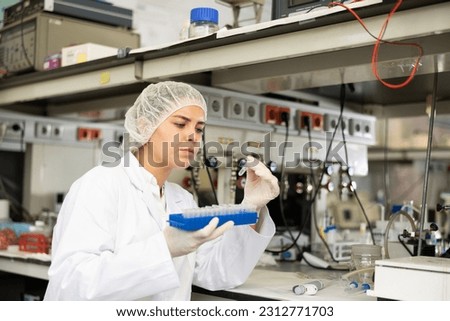 Skilled young female biochemist holding tripod and examining solution in test tube for chemical reaction in research center