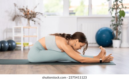 Skilled young female teacher demonstrating seated forward bend pose of yoga in training room - Powered by Shutterstock