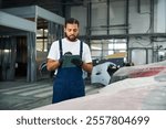 Skilled young man examines vehicle details and takes notes in a well equipped auto repair shop