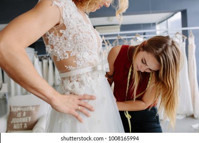 Skillful Dress Designer Fitting Wedding Gown To Woman In Her Boutique. Woman Making Adjustments To Bridal Gown In Fashion Designer Studio.