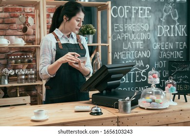 Skillful Female Cafe Worker Looking At Screen Of Pos Machine. Lady Coffeehouse Staff Holding Checkbook And Writing Note In Bar Counter Of Cafeteria. Female Waitress Checking Order On Terminal.