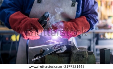 Skillful metal worker working with arc welding machine in factory while wearing safety equipment. Metalwork manufacturing and construction maintenance service by manual skill labor concept.