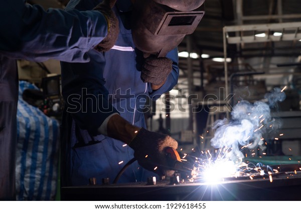 Skillful metal worker working with arc welding\
machine in factory while wearing safety equipment. Metalwork\
manufacturing and construction maintenance service by manual skill\
labor concept.